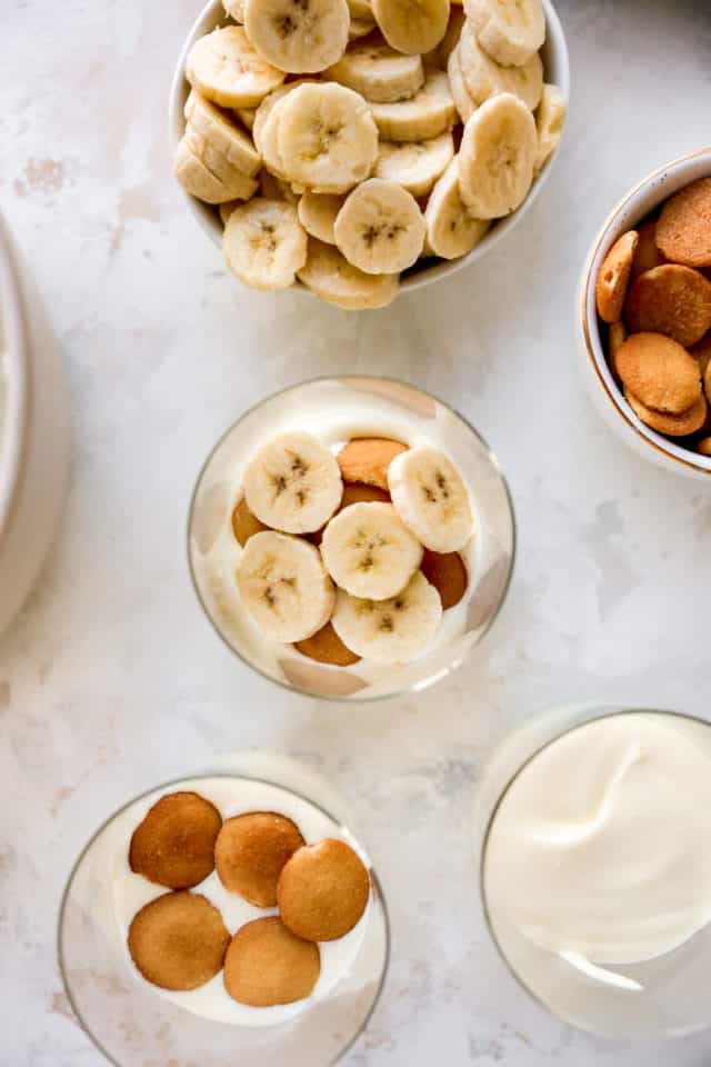 Topping banana pudding in cups with banana slices and cookies.