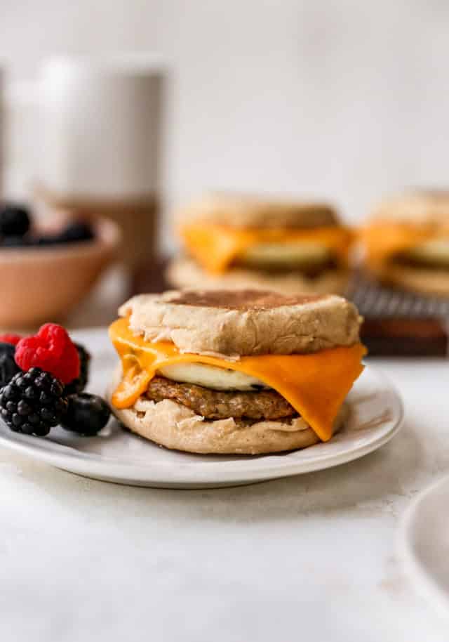 sausage, egg and cheese breakfast sandwich on a white plate with berries