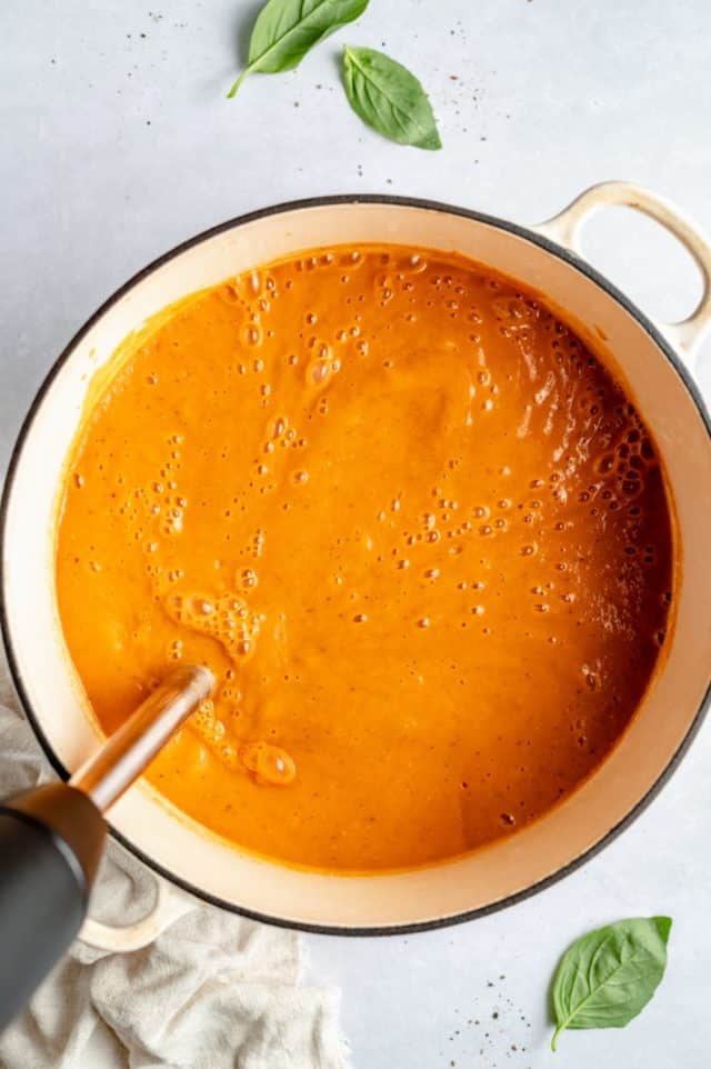 using an immersion blender to blend roasted tomatoes for soup