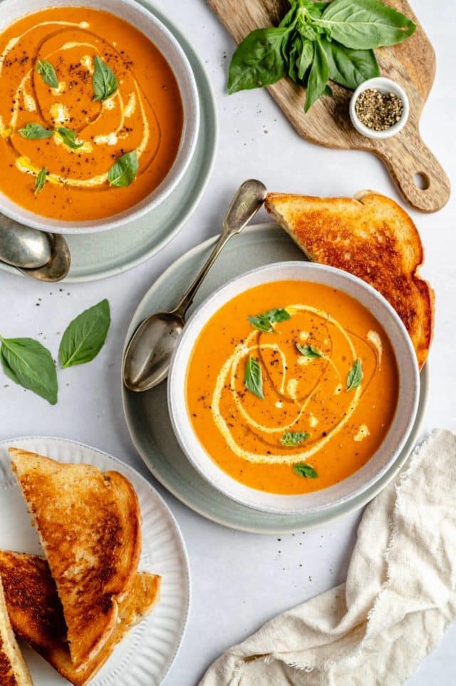 bowls of roasted tomato soup served with grilled cheese and fresh basil