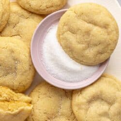 Sugar cookies on a plate with one dipped in a small bowl of sugar.