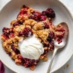 Serving of blackberry crumble topped with a scoop of vanilla ice cream.