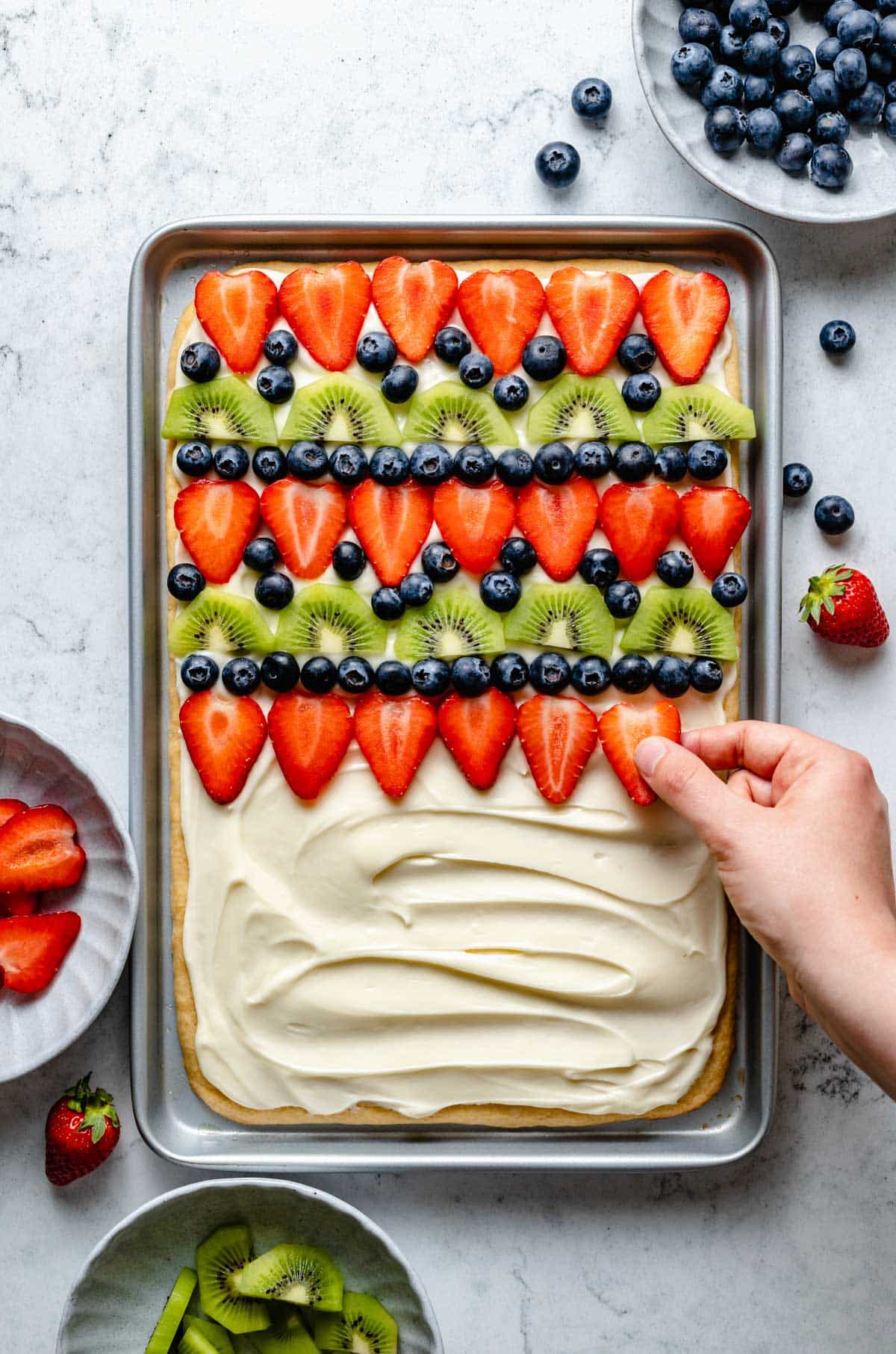 Topping a sugar cookie fruit pizza with sliced strawberries.