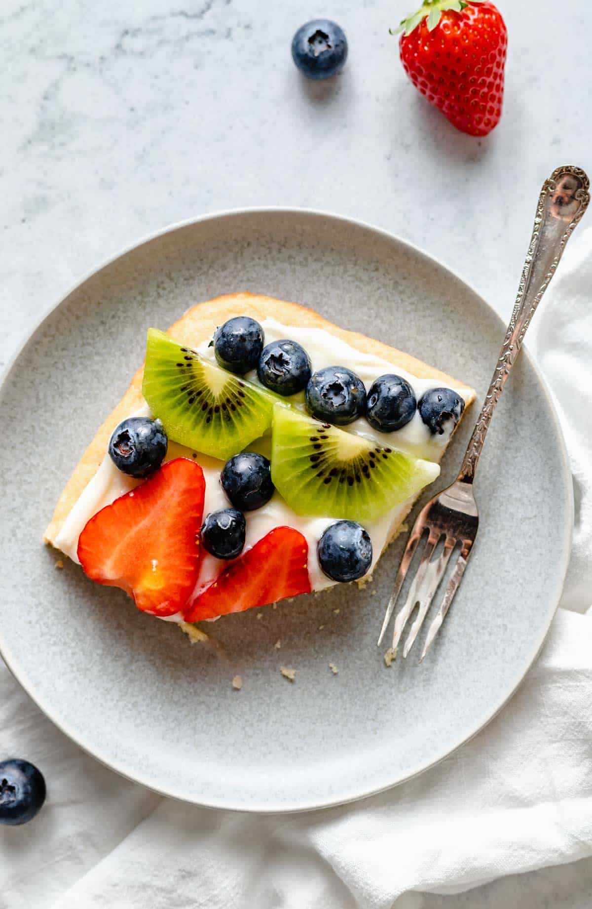 serving of half eaten fruit cookie pizza on a plate with a fork