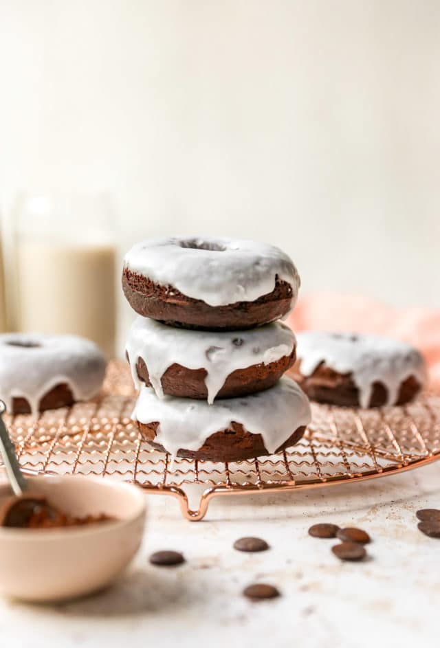 3 glazed chocolate donuts stacked on a wire cooling rack