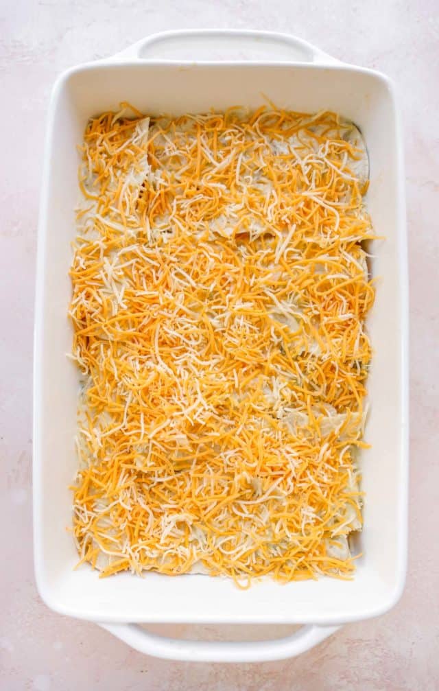 adding shredded cheese over the top of rolled tortillas 
