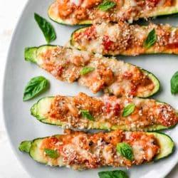 Zucchini stuffed with meat, tomato and cheese on a white serving plate.