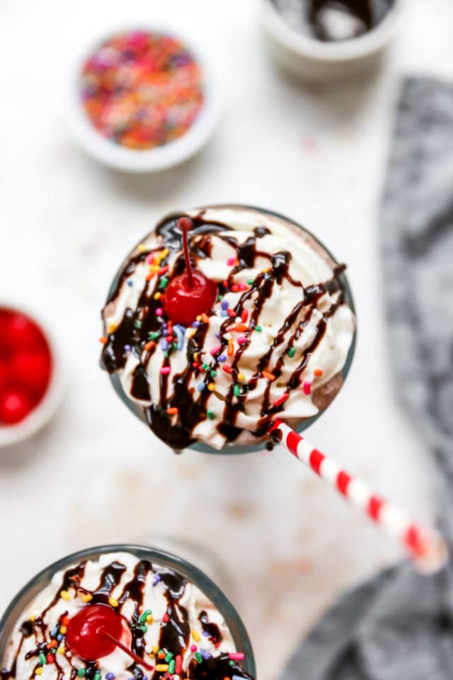 milkshake topped with whipped cream, chocolate syrup, sprinkles and a cherry, served with a straw