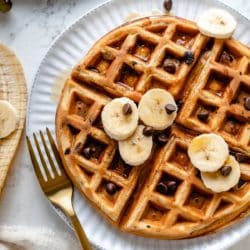 banana waffles topped with chocolate chips, banana slices and maple syrup