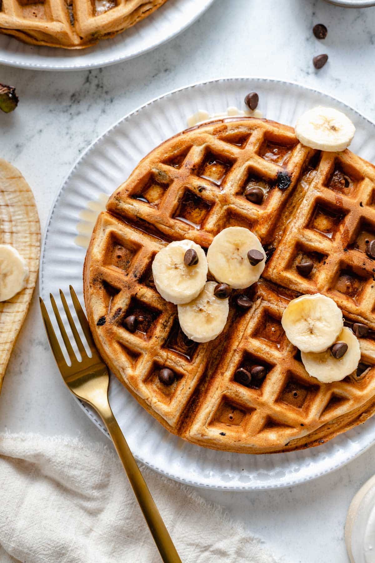 Banana waffles topped with chocolate chips, banana slices and maple syrup.