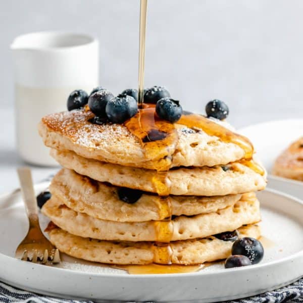 drizzling maple syrup over a stack of fluffy blueberry pancakes