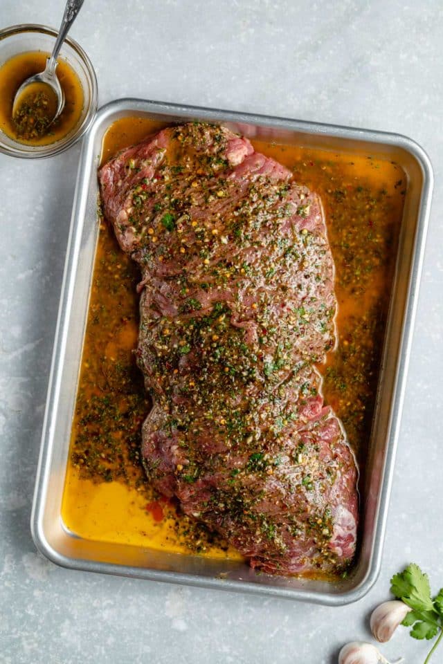 flank steak marinating in a large pan