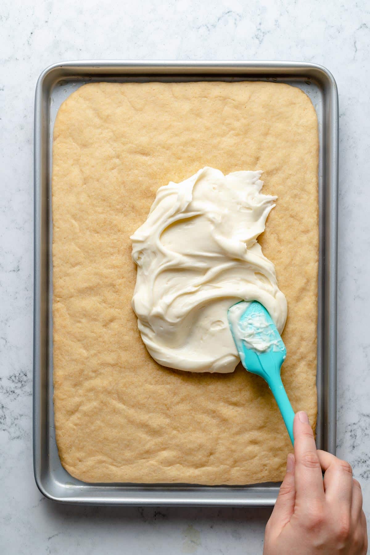 Spreading cream cheese frosting over sugar cookie crust.