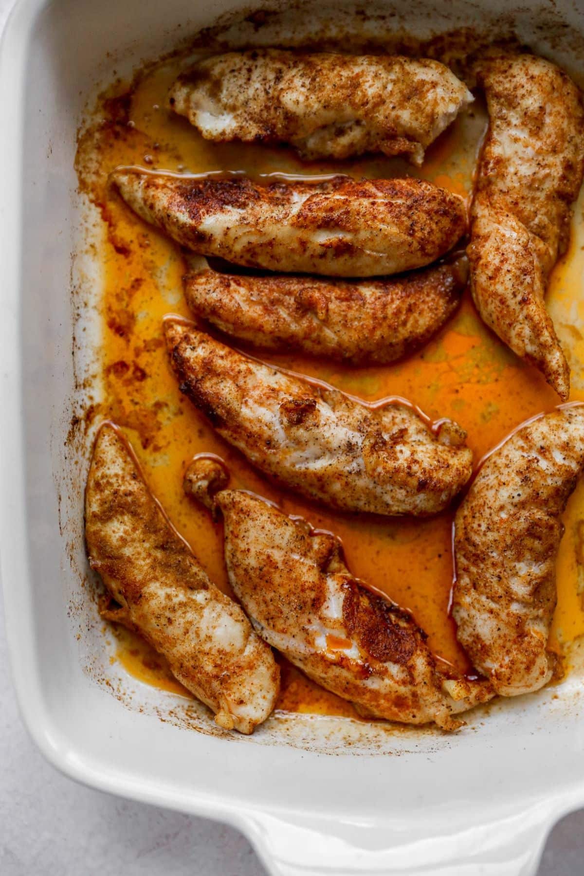 Seasoned chicken tenders in a white baking dish.