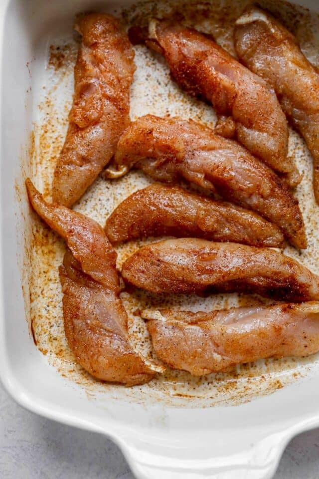 Raw chicken tenders seasoned in a white dish.