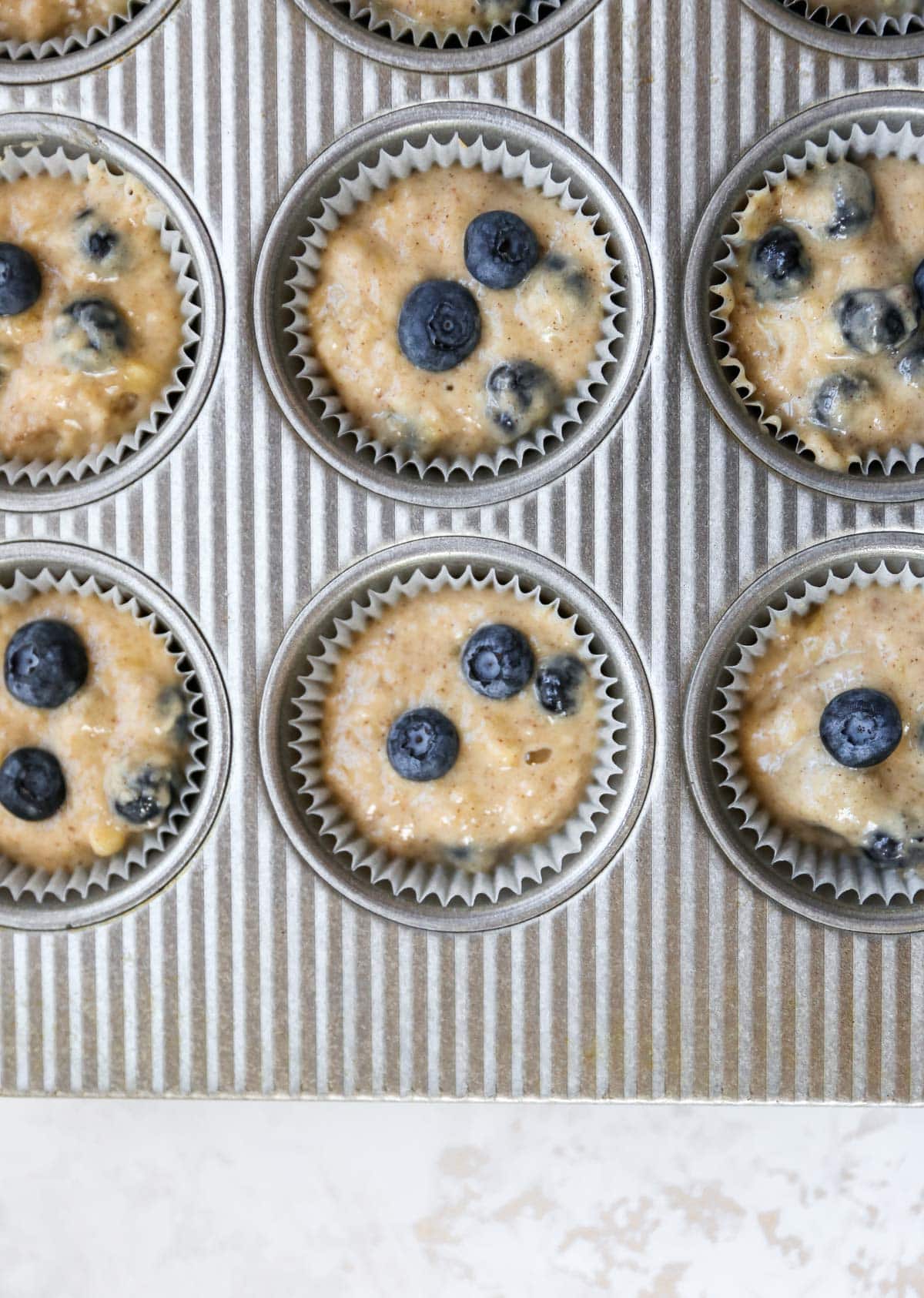 Filling muffin tin with blueberry muffin batter.