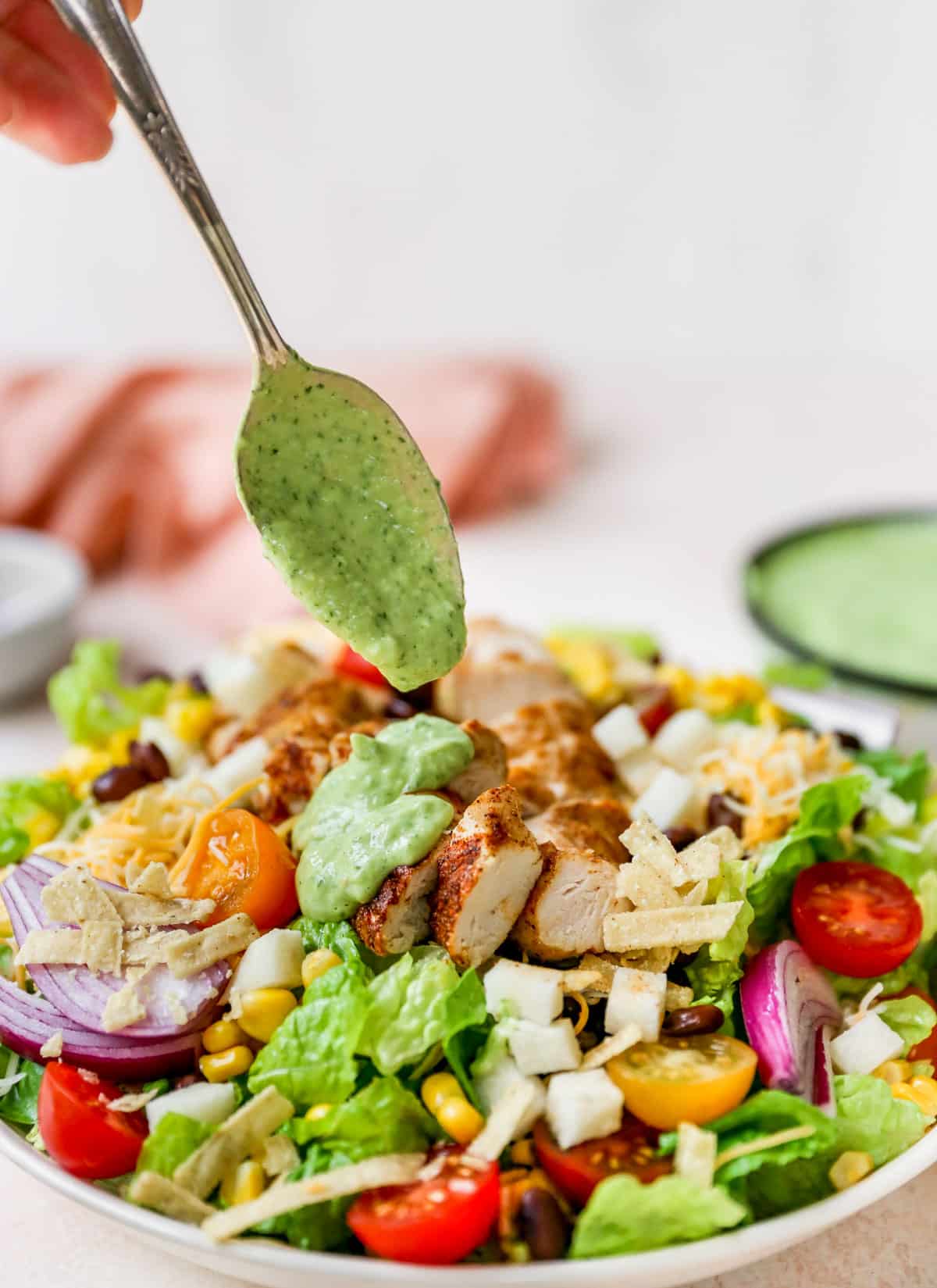 drizzling southwest salad dressing over a salad topped with chicken