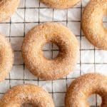 Apple cider donuts covered in cinnamon and sugar on a wire cooling rack.