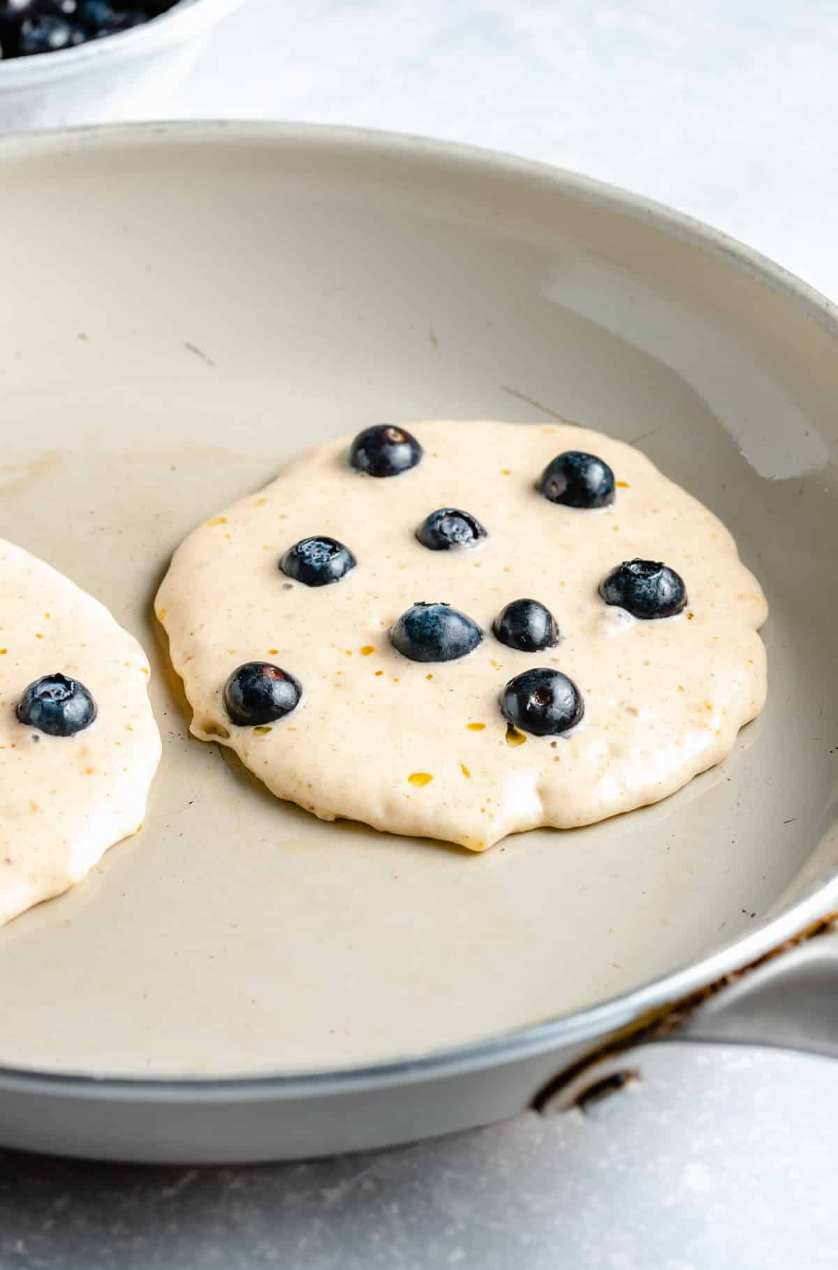 Pancake batter on a skillet topped with blueberries.