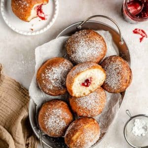 jelly donuts dusted with powdered sugar on a serving tray