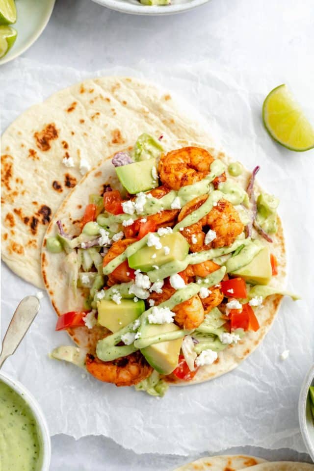 tacos made with seasoned shrimp, fresh slaw, avocado, and tomatoes with a drizzle of sauce