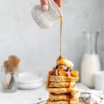 Drizzling maple syrup over a stack of apple pancakes.