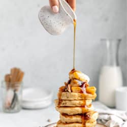 Drizzling maple syrup over a stack of apple pancakes.