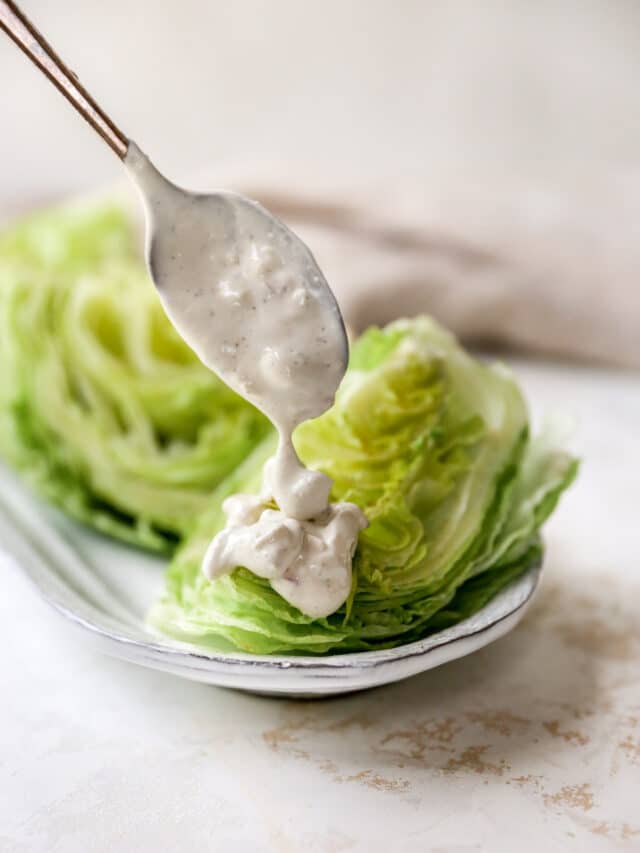 drizzling blue cheese dressing on a wedge of lettuce