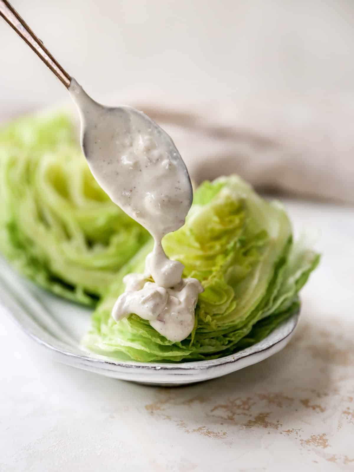 Drizzling blue cheese dressing on a wedge of lettuce.
