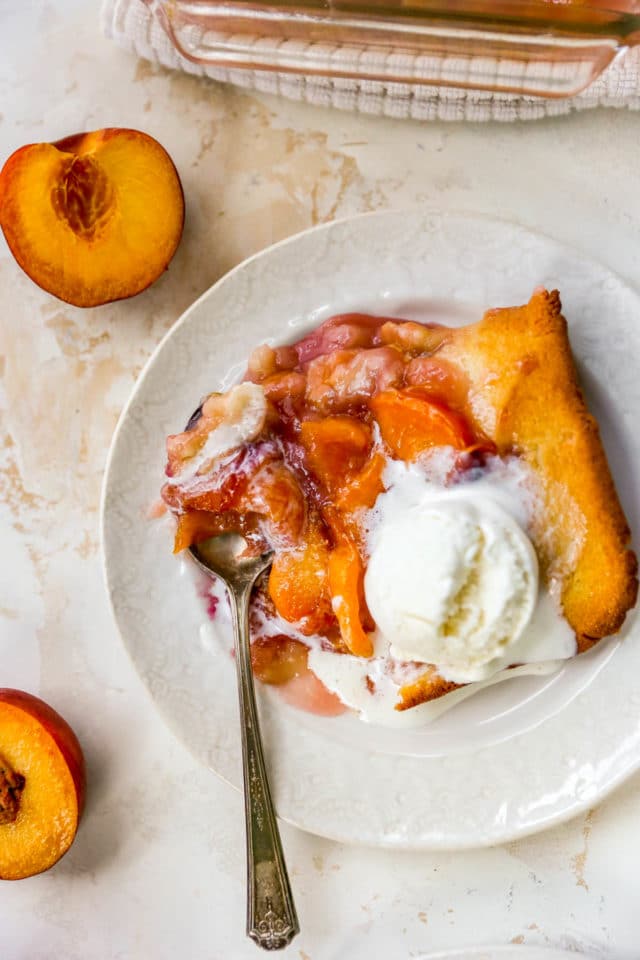 serving of peach cobbler on a plate with a scoop of ice cream melting over the top