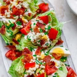 wedge salad on a serving platter topped with fresh tomatoes, bacon and dressing