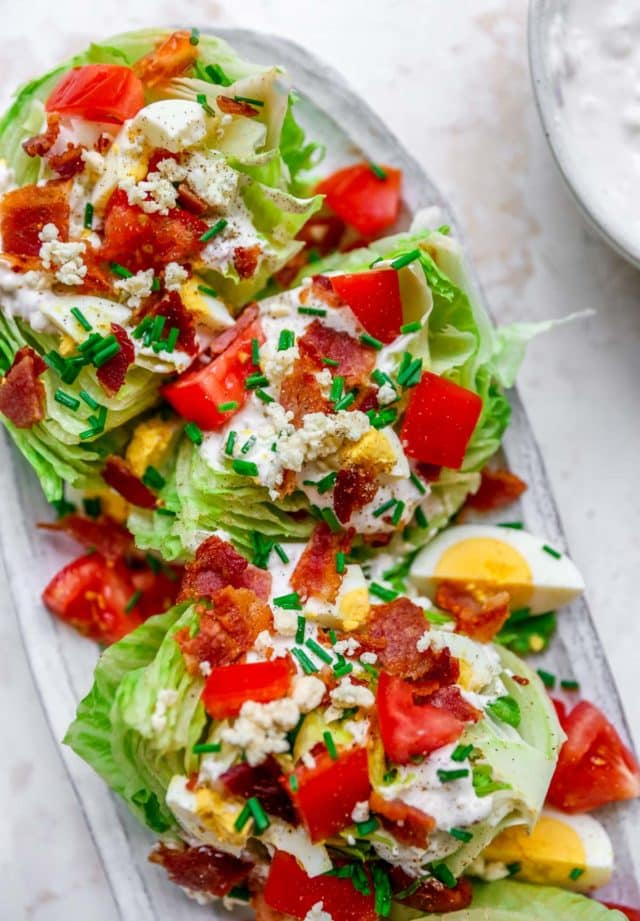 wedge salad on a serving platter topped with fresh tomatoes, bacon and dressing