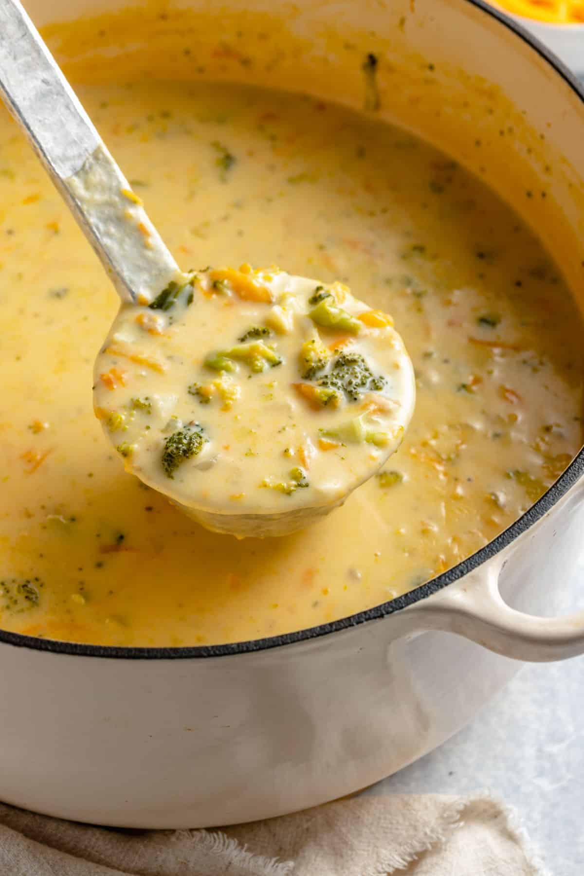 using a ladle to serve broccoli cheese soup out of a large pot