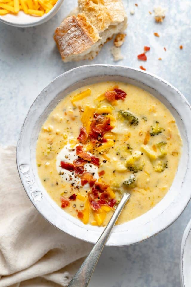 bowl of broccoli cheese soup topped with bacon, sour cream and shredded cheese