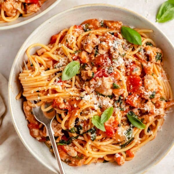 pasta with sausage served in a small white bowl with a fork