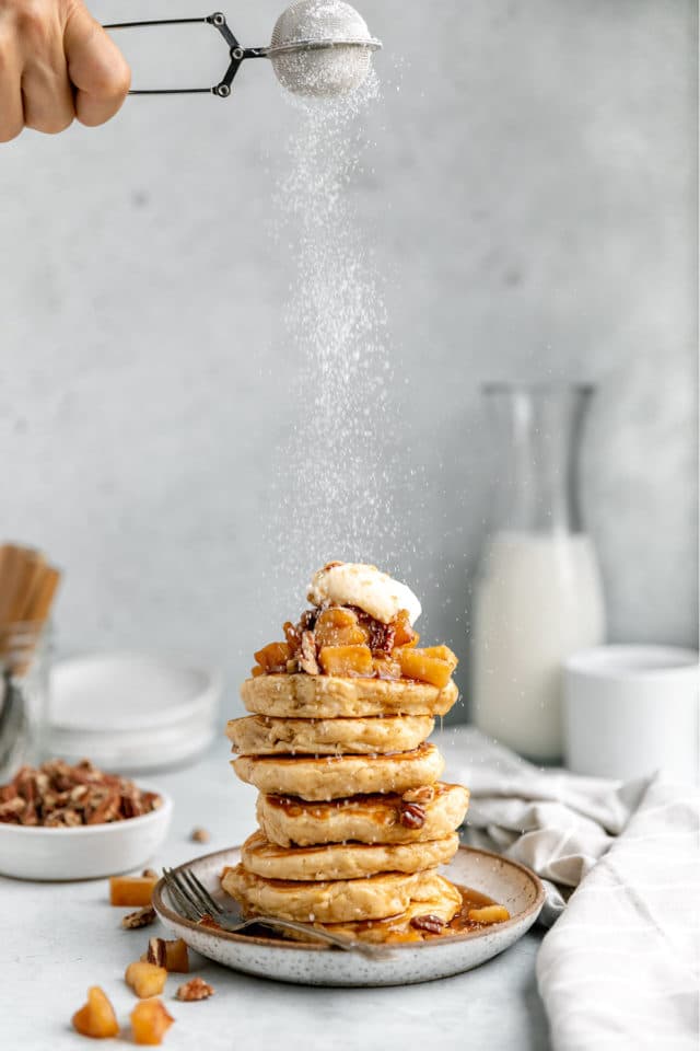 dusting powdered sugar over the top of a stack of pancakes