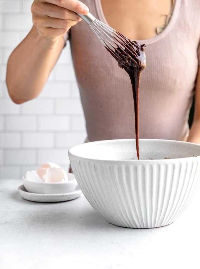 woman whisking chocolate in a white mixing bowl