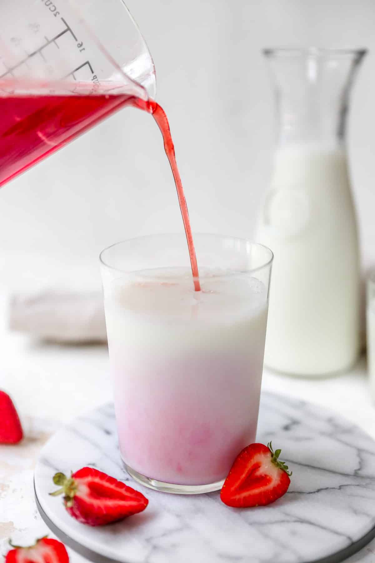 Pouring strawberry syrup into milk to make strawberry milk.