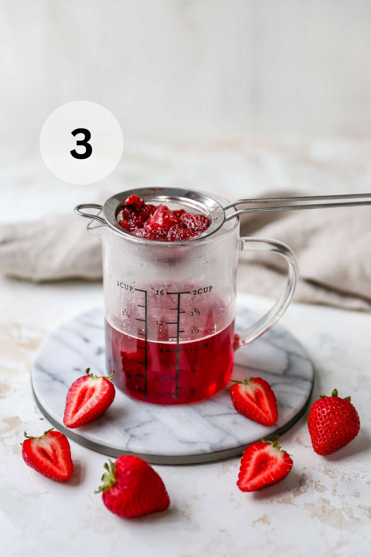 Straining strawberries over a glass measuring cup.