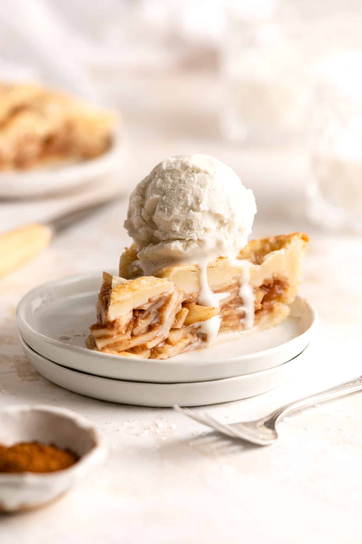Slice of pear pie on a small white plate topped with vanilla ice cream.