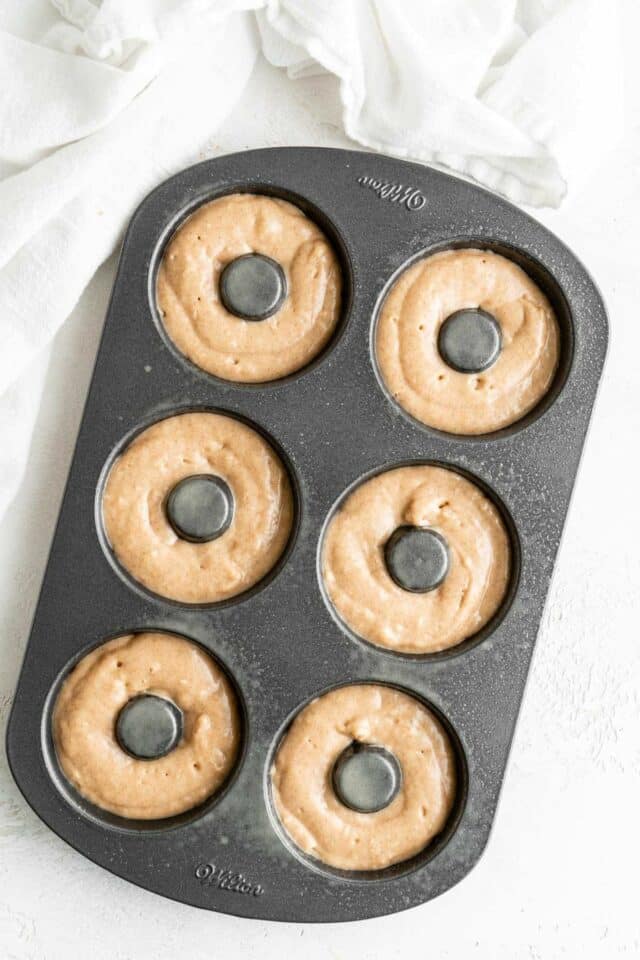 Adding donut batter to a donut pan.