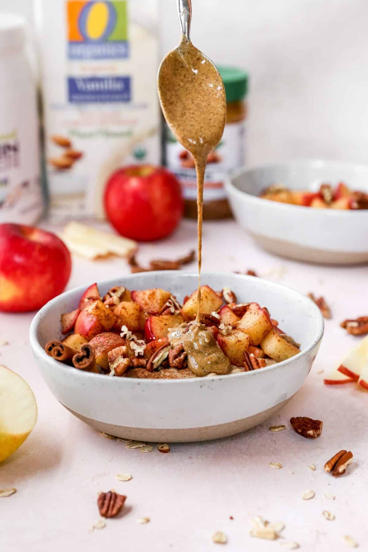 Drizzling almond butter over a bowl with apples and oatmeal.