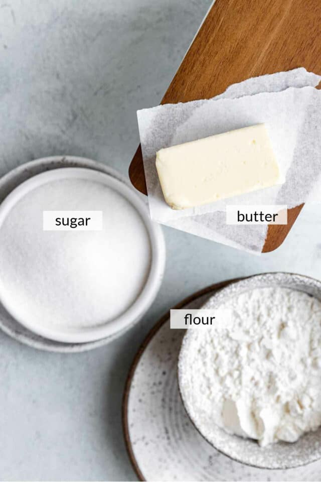 Flour and sugar in a bowl and butter on parchment paper.