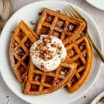 Pumpkin waffles on a white plate served with yogurt, chopped pecans and syrup.