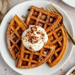 Pumpkin waffles on a white plate served with yogurt, chopped pecans and syrup.