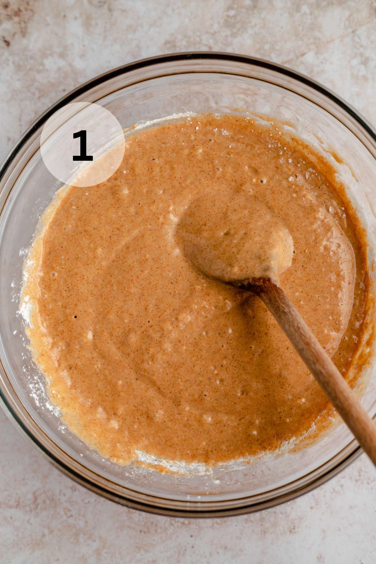 Using a wooden spoon to stir waffle batter in a large glass bowl.
