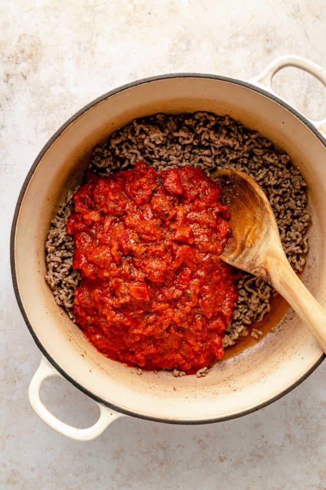 Stirring marinara sauce in with ground beef in a pot.