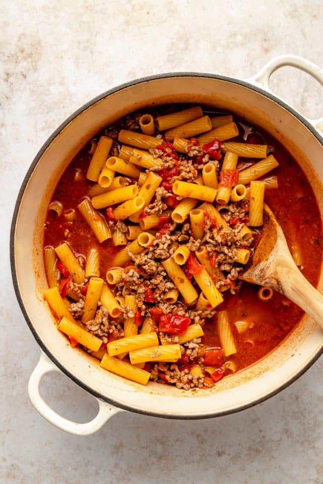 Making one pot pasta in a Dutch oven with noodles and meat sauce.