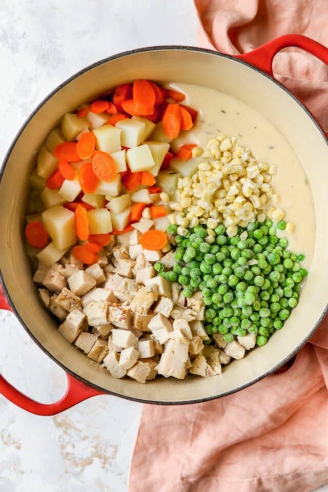 Adding chicken, carrots, potatoes, peas and corn to gravy in a pot.