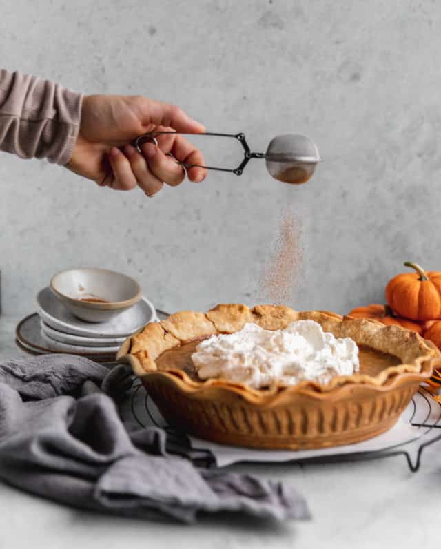 Sprinkling cinnamon over a pie topped with whipped cream.
